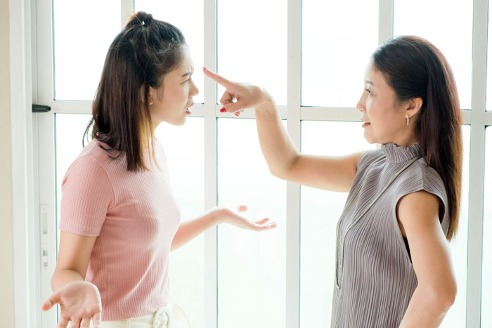 Two sisters arguing indoors near a window, highlighting tension in sister wedding money culture and family dynamics.