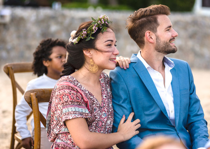 Woman with floral crown and patterned dress embraces man in blue suit, capturing sister wedding money culture moments outdoors.