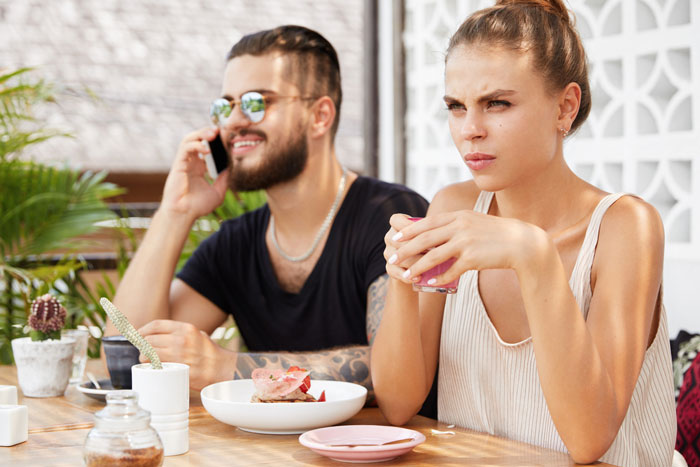 Young woman looks annoyed while her husband talks on phone, highlighting guy's affection for his sick wife tension. Young woman looks annoyed while her husband talks on phone, highlighting guy's affection for his sick wife tension.
