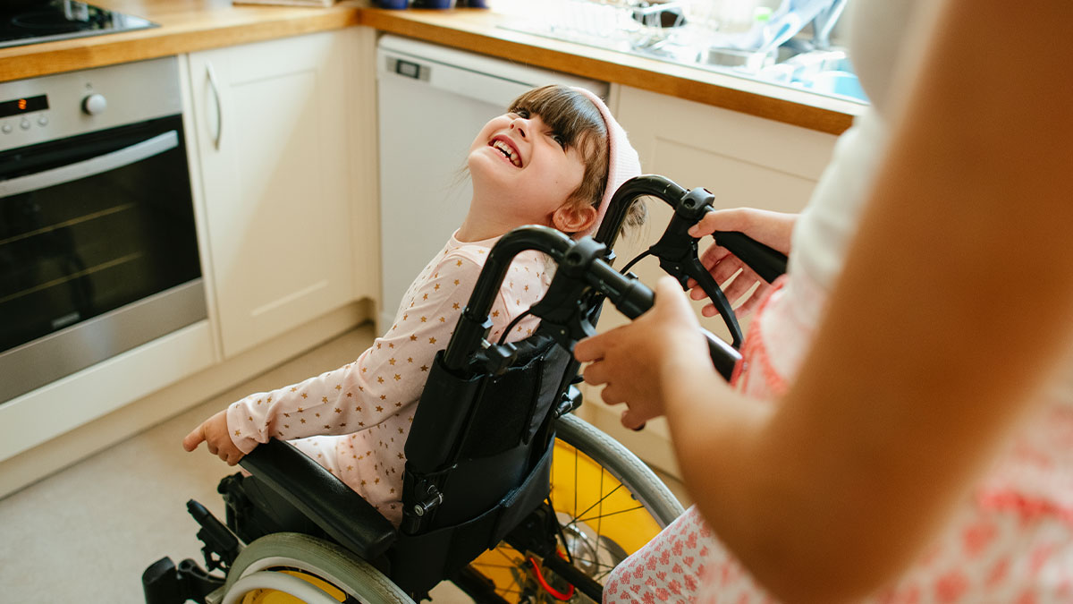 Young woman in a wheelchair being pushed joyfully by a family member in a bright kitchen during a housewarming party.