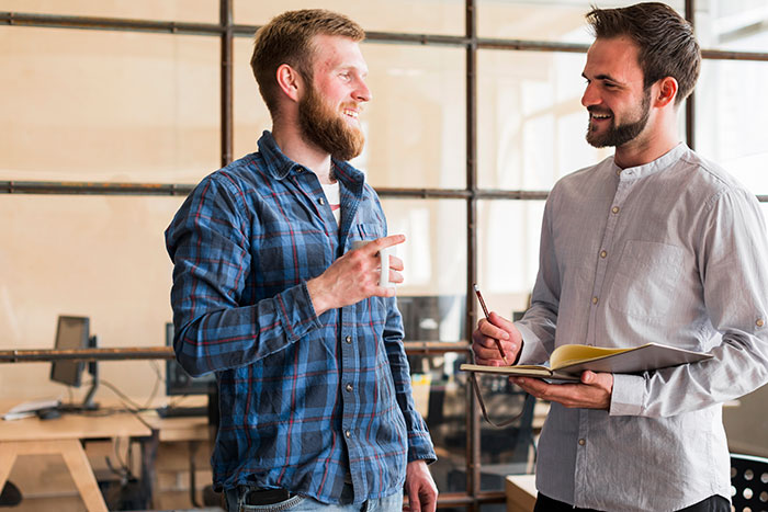 Two men discussing and smiling in an office setting, illustrating lies that had a bigger effect on people’s lives.