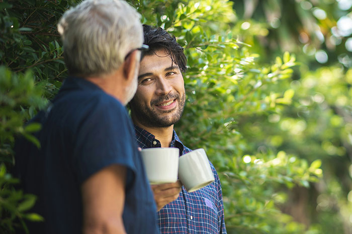 Two men holding coffee mugs, engaged in a meaningful conversation outdoors, reflecting on lies with big life impact.