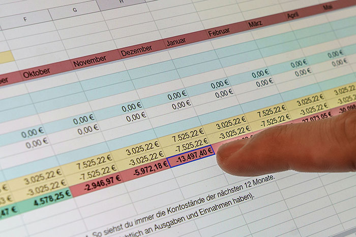 Finger pointing at negative values in a financial spreadsheet highlighting the impact of lies on people's lives and finances.