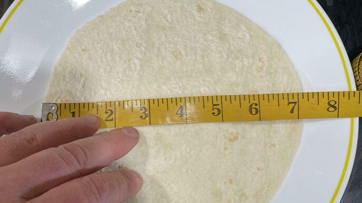 Hand measuring tortilla with tape measure showing sneakflation impact on product size reduction.
