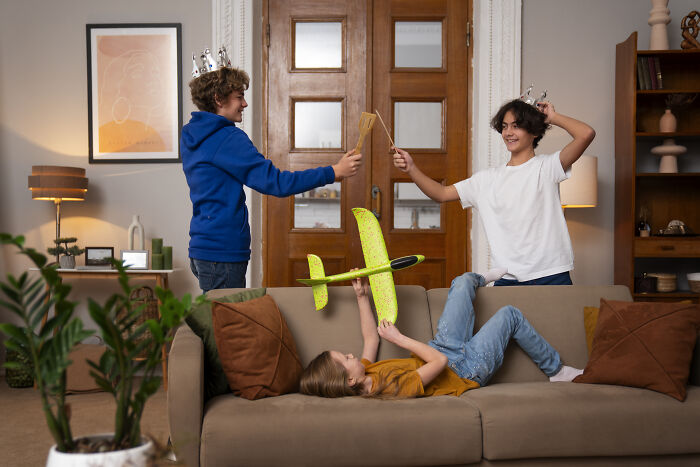 Three children playing with toy swords and a glider airplane on a couch during a family visit at home. Three children playing with toy swords and a glider airplane on a couch during a family visit at home.