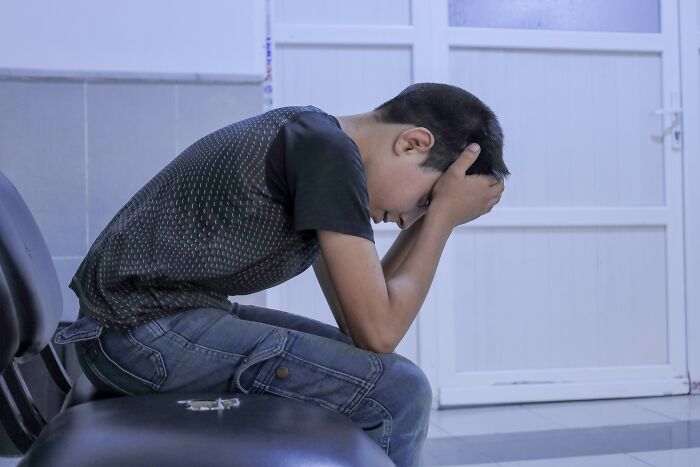 Teen boy sitting with head in hands, showing pain from sprain and c*****d ribs during family visit incident. Teen boy sitting with head in hands, showing pain from sprain and c*****d ribs during family visit incident.