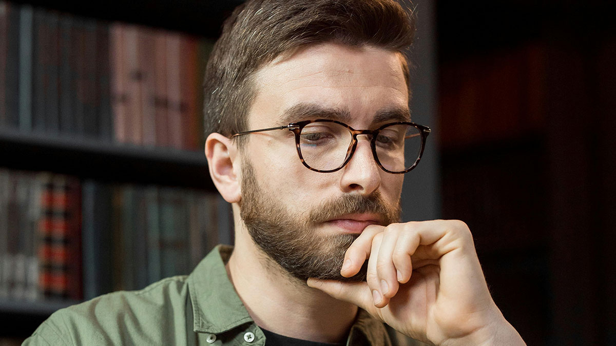 Young man with glasses and beard looking thoughtful while researching HOA president secrets at home.