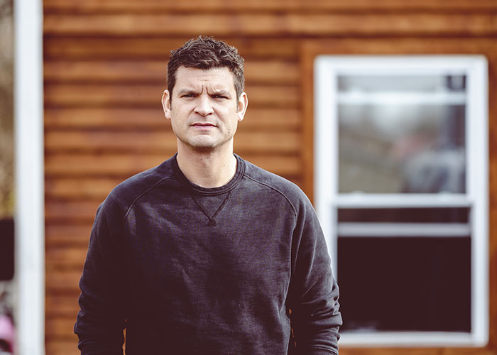 Man standing outside wooden house, looking determined after dealing with stalkerish HOA president and court victory. Man standing outside wooden house, looking determined after dealing with stalkerish HOA president and court victory.
