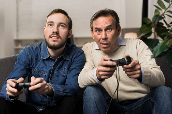 Stepdad and son playing video games together, stepdad trying to connect while kids stay loyal to bio dad’s influence.