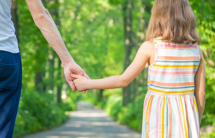 Child holding hands with adult in a park, representing stepdad trying to connect while bio dad remains in kids’ hearts.