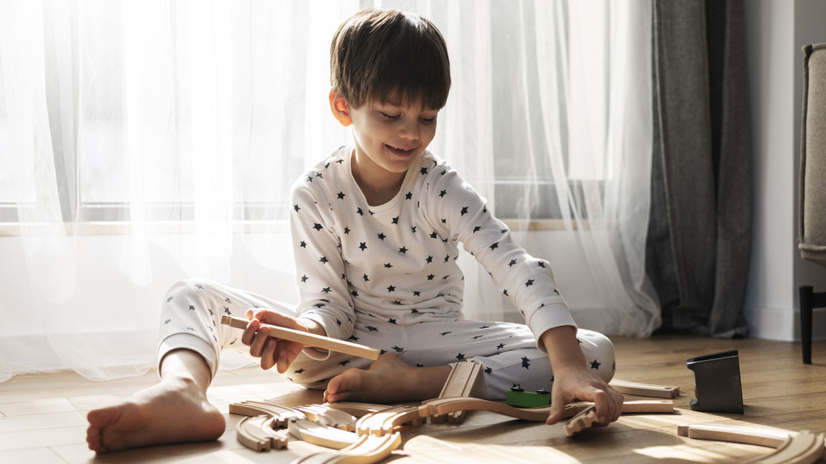 Young boy in star pajamas playing with wooden train tracks on the floor, illustrating bizarre events that defy logic.