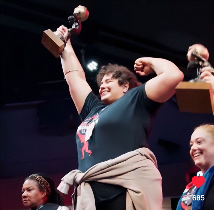 Woman holding trophy and celebrating on stage at strongwoman competition, highlighting world’s strongest woman controversy. Woman holding trophy and celebrating on stage at strongwoman competition, highlighting world’s strongest woman controversy.