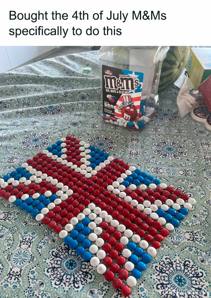 Red white and blue M&M candies arranged in a British flag pattern on a patterned table with stupid food memes theme.