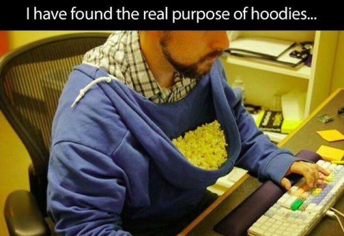 Man wearing a blue hoodie filled with popcorn while typing on a keyboard in a humorous food meme for stupid people.