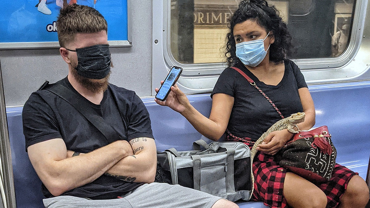 Man with face covering and woman with mask holding a lizard on NYC subway in a captivating street portrait.