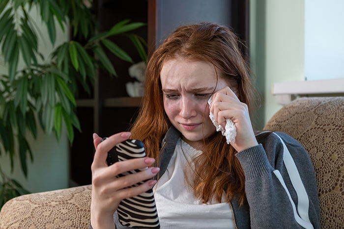 Sad young woman wiping tears while holding phone, reflecting sibling refuse newborn nephew care emotional distress. Sad young woman wiping tears while holding phone, reflecting sibling refuse newborn nephew care emotional distress.