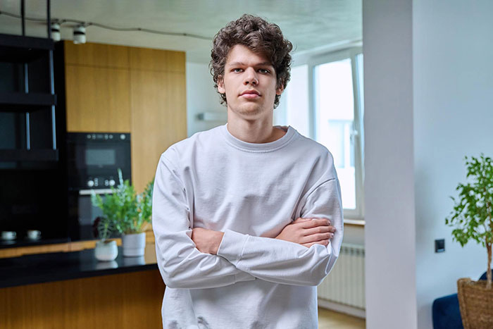 Young man in casual white sweatshirt with arms crossed, looking frustrated in a modern kitchen setting. Young man in casual white sweatshirt with arms crossed, looking frustrated in a modern kitchen setting.