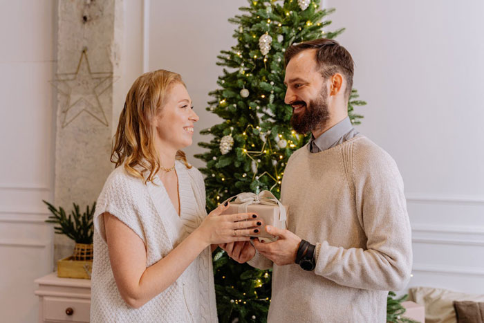 Couple exchanging a Christmas gift near decorated tree, highlighting man thinking proposal counts as holiday gift. Couple exchanging a Christmas gift near decorated tree, highlighting man thinking proposal counts as holiday gift.