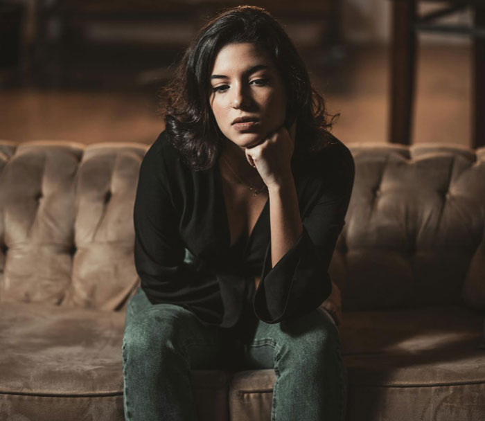 Woman sitting on a couch looking thoughtful and disappointed, representing a man’s proposal not counting as a Christmas gift reality check. Woman sitting on a couch looking thoughtful and disappointed, representing a man’s proposal not counting as a Christmas gift reality check.