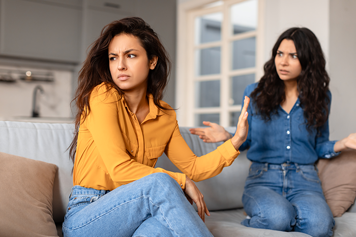 Two women arguing on a couch, one frustrated after borrowing a car and keeping it longer than agreed.