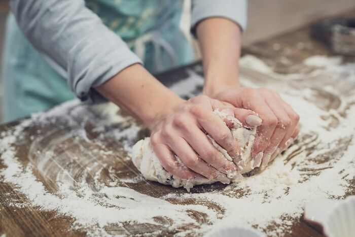 Hands kneading dough on a floured wooden surface demonstrating common home cook mistakes in sharpening knives.