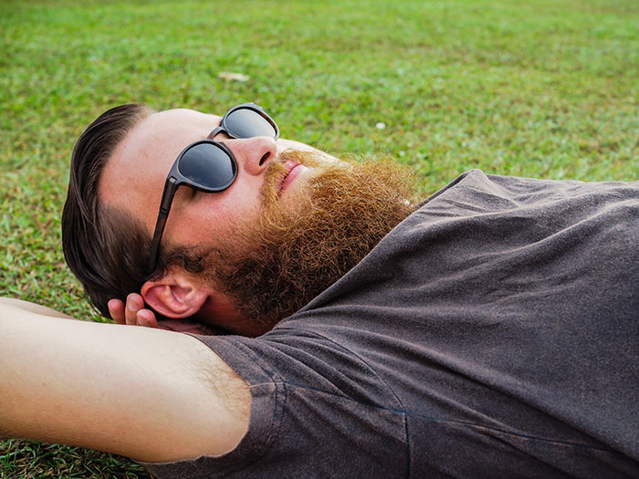 Bearded man wearing sunglasses lying on grass, reflecting on thoughts men anonymously wish to reveal without judgment.