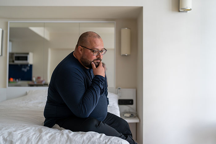Man sitting on bed in a bedroom, looking thoughtful and reflective, expressing emotions men wish to reveal anonymously.