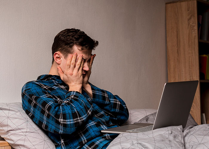 Young man in a blue plaid shirt covering his face while using a laptop, revealing thoughts men wish they could say without judgment