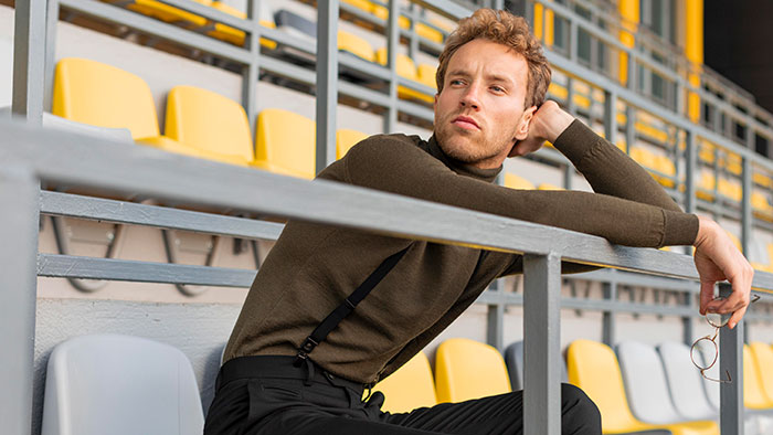 Young man sitting in stadium seats, looking pensive and thoughtful, representing men anonymously revealing secrets.