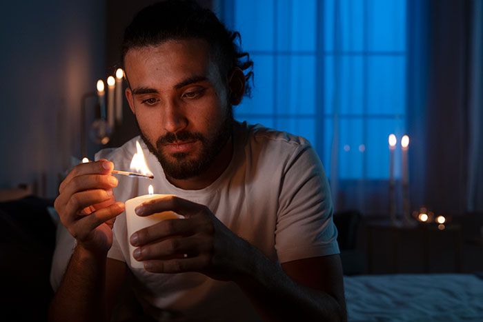Man lighting a candle in a dim room, symbolizing men anonymously revealing their thoughts without being judged.
