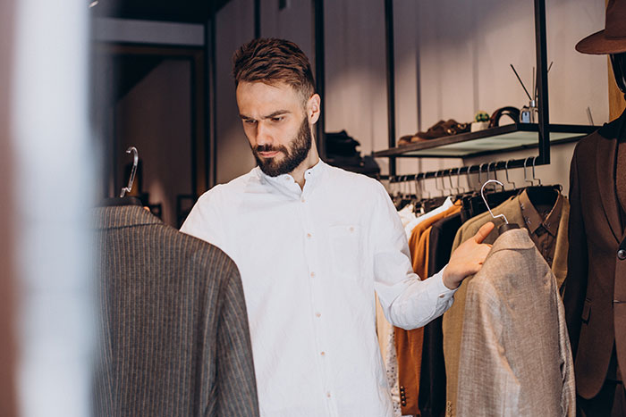 Man with beard choosing suits in a clothing store, reflecting the theme of men anonymously revealing personal thoughts.