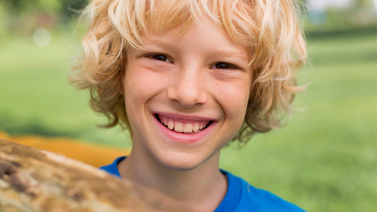 Smiling young boy with blonde hair outdoors, representing themes only adopted people understand and childhood joy.