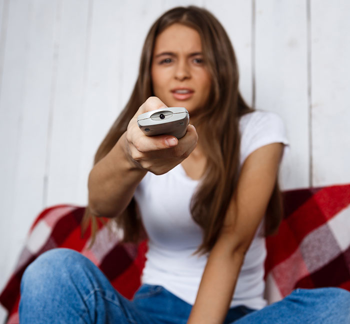 Young woman holding a remote control focused on TV, representing the concept of metal detectors at school in American culture.