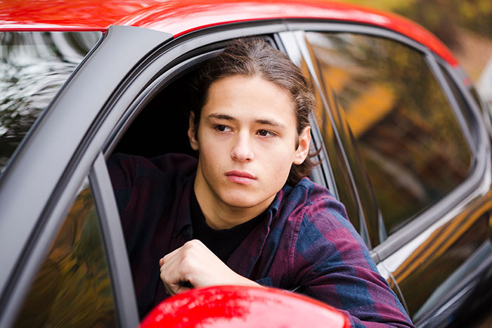 Teen boy looking thoughtfully out car window, symbolizing concerns about metal detectors at school in America.