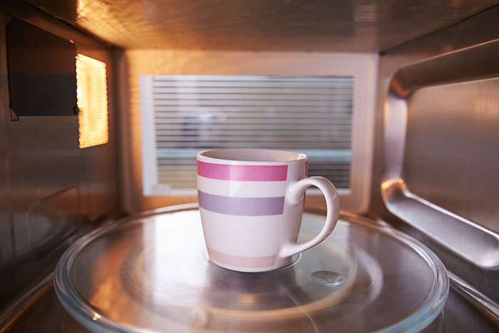 A ceramic mug with pink and purple stripes heating inside a microwave oven in a kitchen setting.