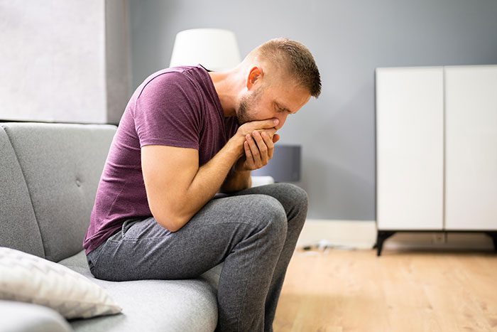 Man sitting on a couch looking stressed and anxious, illustrating concerns about metal detectors at school safety.