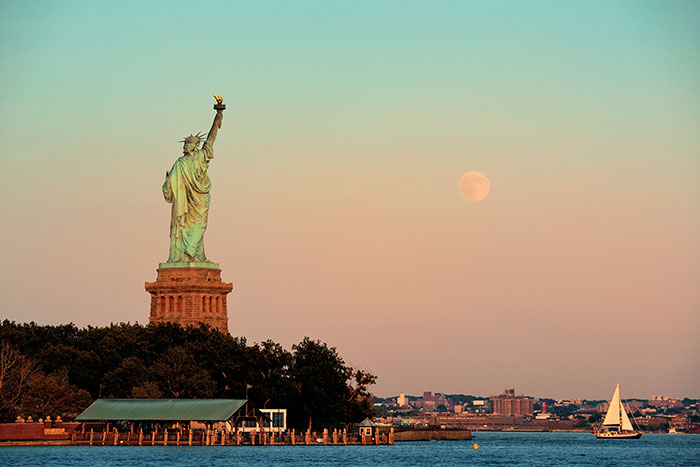 Statue of Liberty at sunset with clear sky and full moon, symbolizing iconic American landmarks and culture.