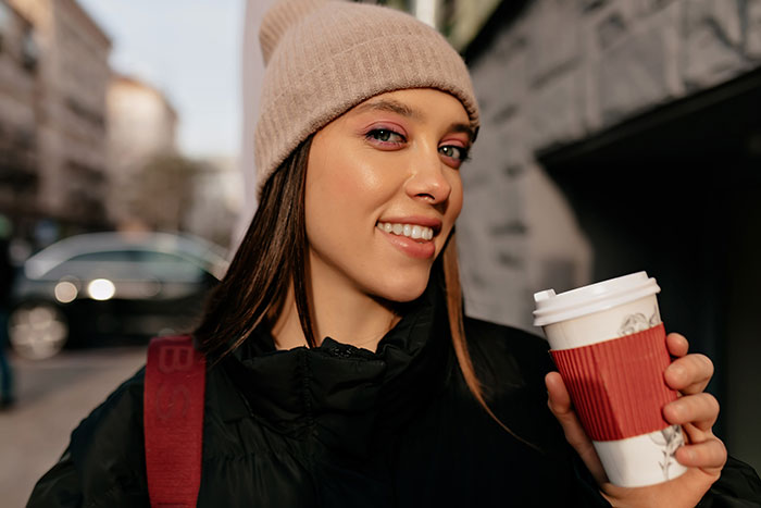 Young woman in a beanie holding a coffee cup outdoors, highlighting the topic of metal detectors at school security challenges.