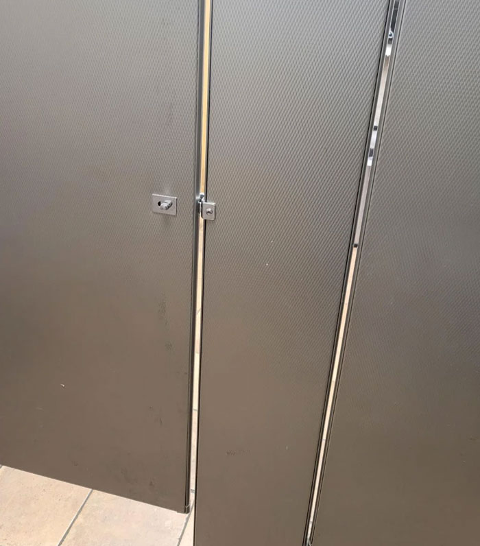 School bathroom stalls with metal locks and slight gaps between the doors, highlighting security measures in schools.