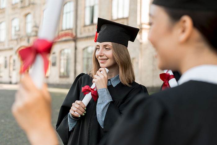 Female students in graduation gowns holding diplomas outside a school building, representing metal detectors at school context.
