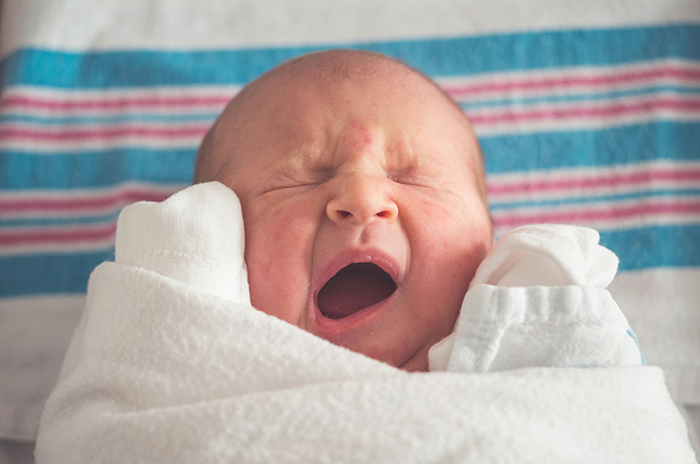 Newborn wrapped in a hospital blanket, yawning while resting peacefully in a bright medical setting. Newborn wrapped in a hospital blanket, yawning while resting peacefully in a bright medical setting.