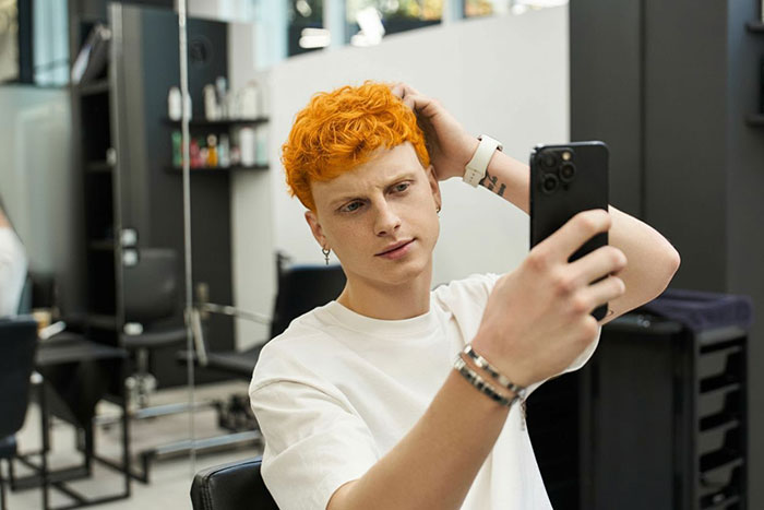 Young man with freshly dyed orange hair taking a selfie in a salon chair, capturing the classmate drama look. Young man with freshly dyed orange hair taking a selfie in a salon chair, capturing the classmate drama look.