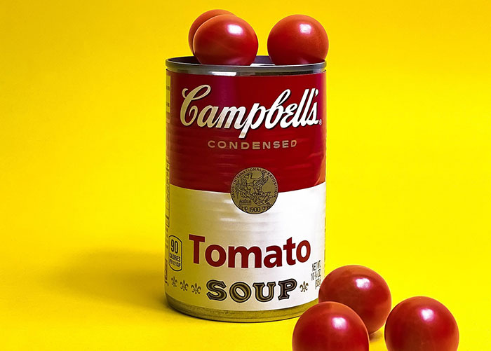 Campbell's tomato soup can with fresh tomatoes on top and beside it against a bright yellow background. Campbell's tomato soup can with fresh tomatoes on top and beside it against a bright yellow background.
