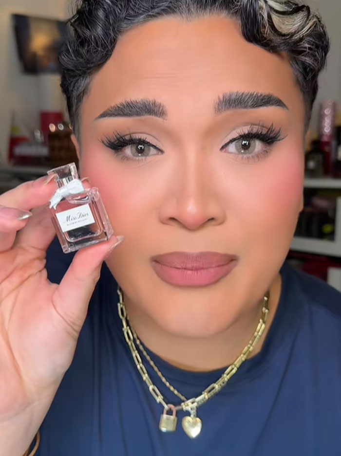 Person holding a tiny Dior perfume bottle, reacting with a puzzled expression, highlighting Dior advent calendar controversy. Person holding a tiny Dior perfume bottle, reacting with a puzzled expression, highlighting Dior advent calendar controversy.