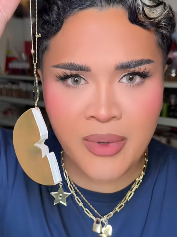 Person with styled hair holding a Dior advent calendar ornament, wearing layered gold necklaces and makeup. Person with styled hair holding a Dior advent calendar ornament, wearing layered gold necklaces and makeup.