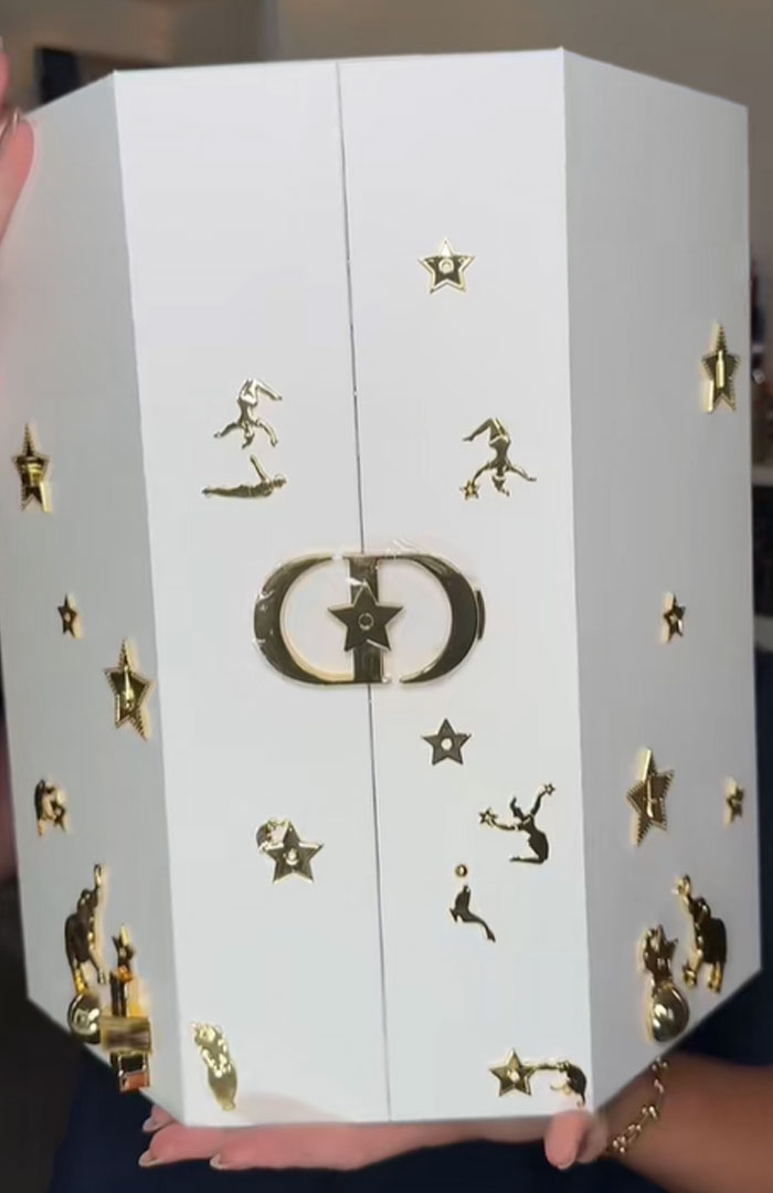 White Dior advent calendar box with gold star and figure decorations held by a person, luxury holiday countdown item. White Dior advent calendar box with gold star and figure decorations held by a person, luxury holiday countdown item.