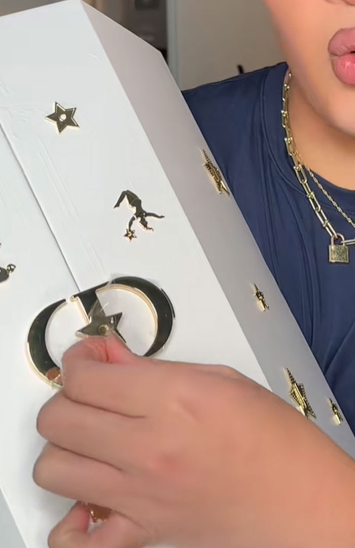 Person holding a white Dior advent calendar with gold star and crescent moon designs, showcasing luxury packaging details. Person holding a white Dior advent calendar with gold star and crescent moon designs, showcasing luxury packaging details.