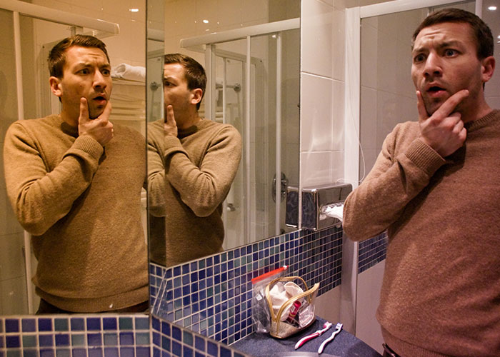Man looking surprised in bathroom mirror, illustrating strange things people accidentally saw neighbors doing.