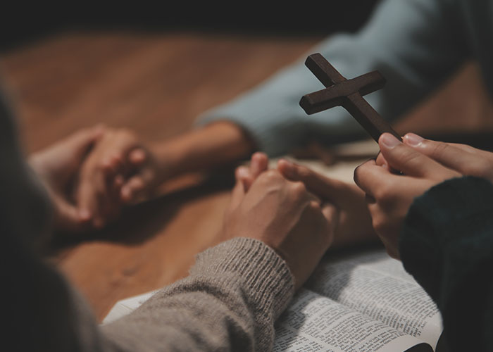 People holding hands and a wooden cross over an open Bible during a quiet moment neighbors accidentally saw.