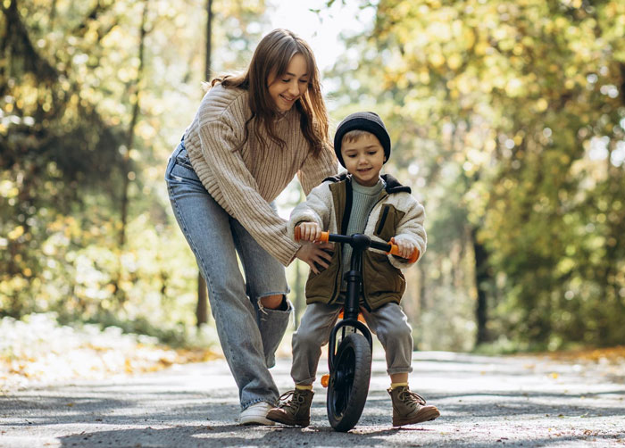Young mother helping her son learn to ride a bike outdoors, highlighting support in parenting moments.